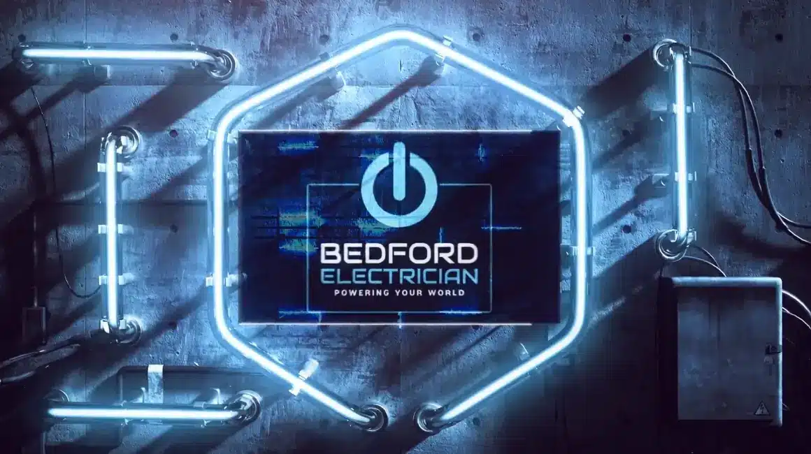 A glowing neon sign in a hexagonal shape with a power symbol and the text "Bedford Electrician - Powering Your World" against a textured wall. The neon lights are blue, creating a futuristic and industrial look, perfect for an electrician in Milton Keynes.
