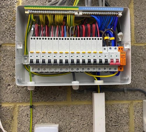 An open electrical panel, reminiscent of The Hayloft's rustic charm, is mounted on a wall, showcasing multiple circuit breakers, switches, and colorful wires organized inside.